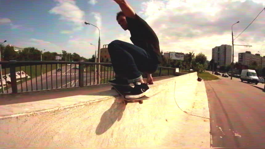 A young man performs a skateboard trick on a concrete ramp in an urban setting in slow motion, shot on a fisheye lens with a vintage VHS effect