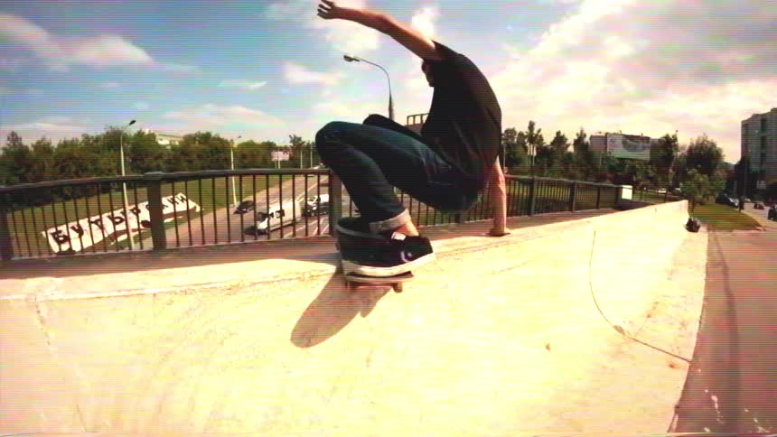 Slow-motion, wide-angle shot of a young man skateboarding and doing a trick on a concrete ramp in an urban setting