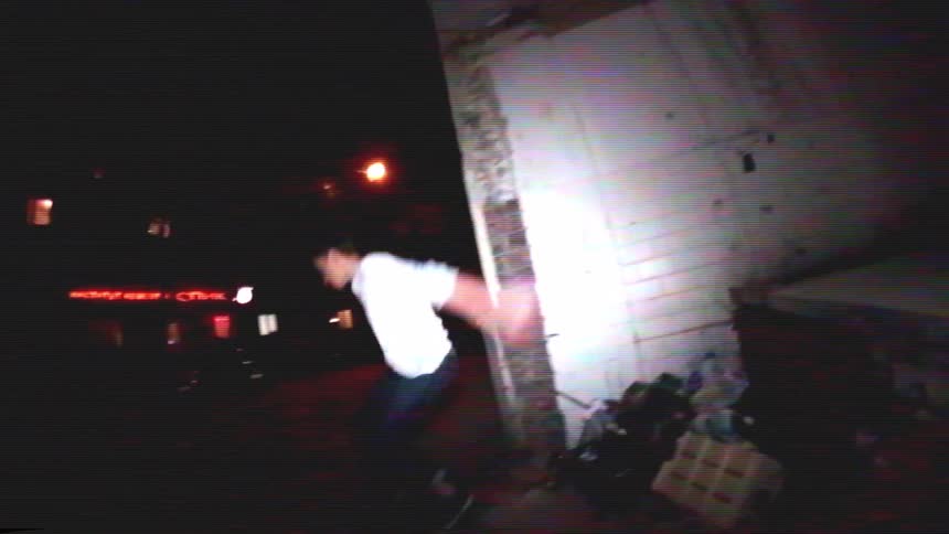 A young man performs a skateboard wallride trick on a dilapidated building at night in the city, filmed in a retro VHS style