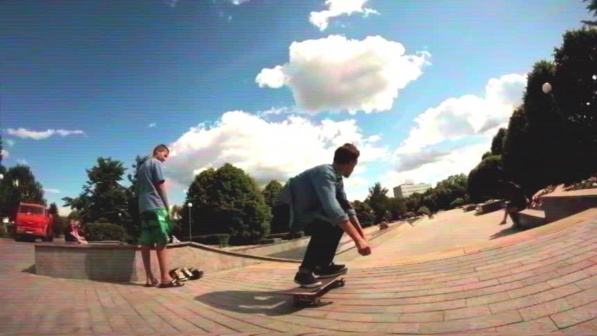 A young man performs skateboarding tricks in slow motion in a sunny urban park, captured with a fisheye lens and a retro aesthetic