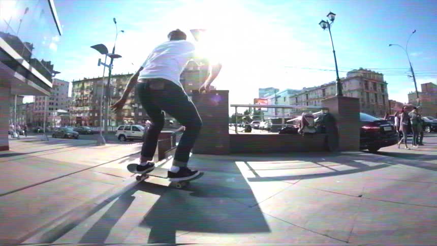 A slow-motion, wide-angle shot of a young man performing a skateboard trick over a flight of stairs in the city