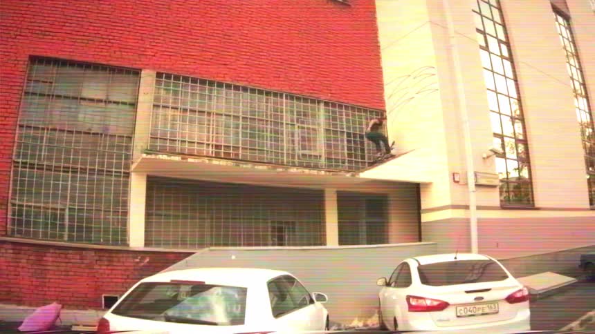 A man on a scooter performs a daring tailwhip trick on a high ledge of a red brick building