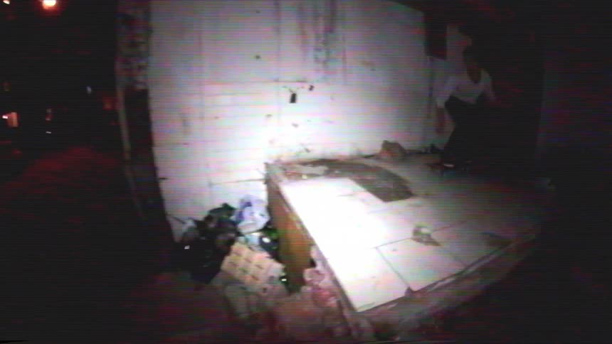 A skateboarder performs a jump trick at night off a dilapidated ledge in a gritty urban alleyway, filmed in a slow motion lo-fi VHS style