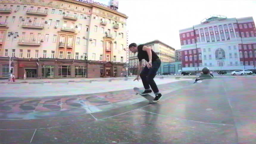 A skateboarder performs a trick in slow motion on a marble monument ledge in a wide city square