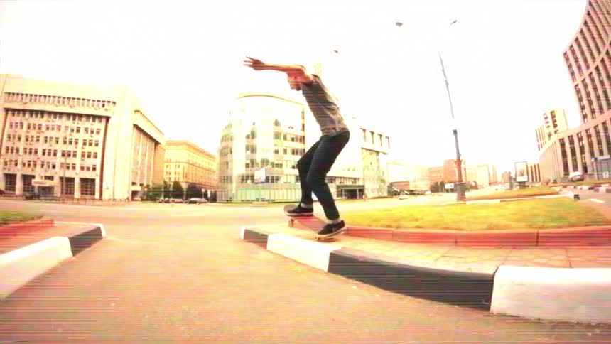 A skateboarder performs a trick in slow motion on a curb in an empty city street with a vintage aesthetic