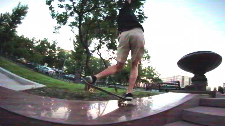 Slow-motion fisheye shot of a skateboarder grinding a curved marble ledge in an urban plaza with a vintage VHS look