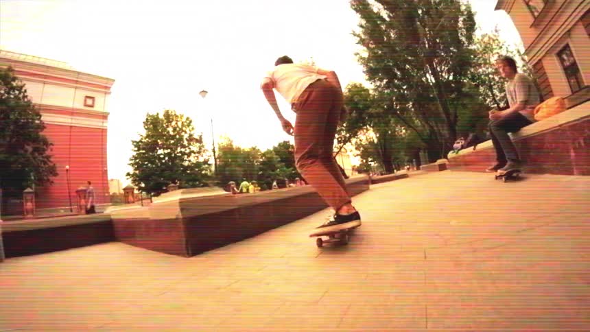 A young skateboarder lands a kickflip and grinds a ledge in a city park, filmed in slow motion with a fisheye lens