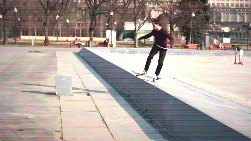 Vintage-style slow motion footage shows a young man skateboarding and landing a trick in a city park