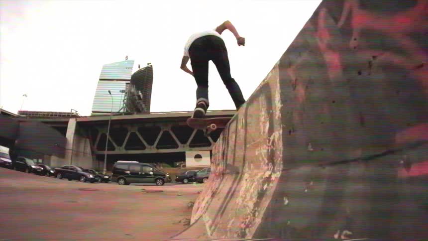 A skateboarder performs a stylish grind on a concrete ramp under a city bridge in slow motion with a vintage VHS aesthetic