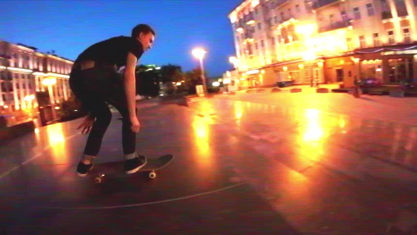 Vintage VHS-style slow-motion footage of a skateboarder doing tricks in a glowing city plaza at night