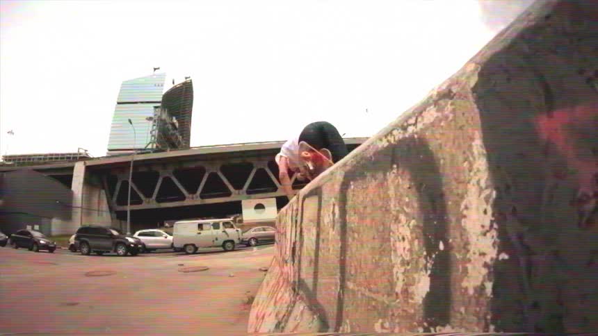 A skateboarder in slow motion grinds along a concrete barrier, bails the trick, and tumbles into a grassy patch below
