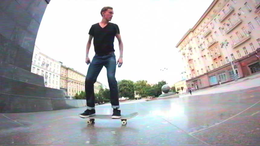 In slow motion, a skateboarder performs a stylish wallride on a monument and a pop shove-it trick in a city square