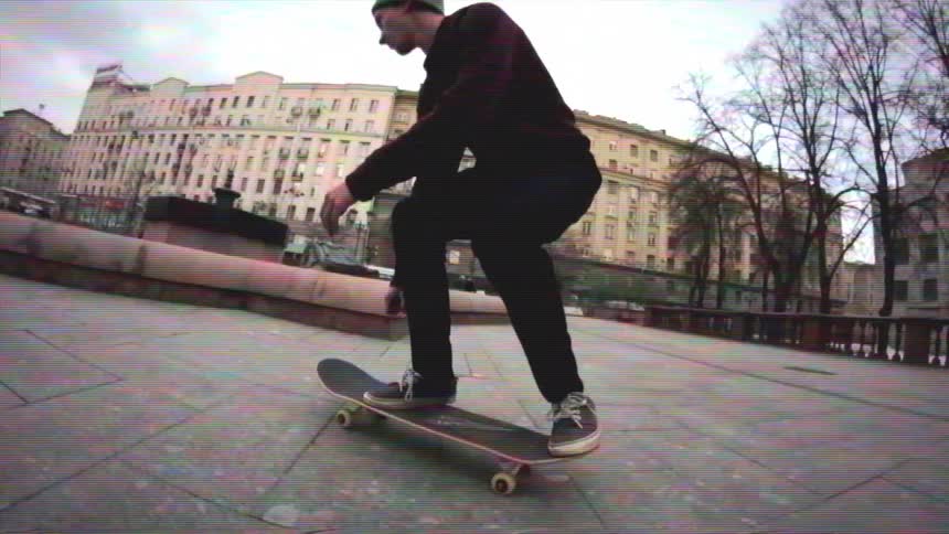 A skateboarder performs a trick in slow motion, jumping into an empty, snowy fountain in a city plaza in this vintage-style clip