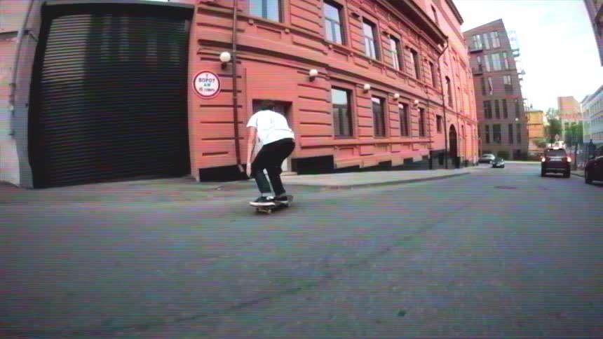 A skateboarder gracefully lands a trick off a city ledge and cruises down the street in a stylish slow-motion wide-angle shot