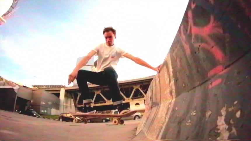 A skateboarder executes a stylish handplant air trick on a concrete ramp in an urban environment, captured in super slow motion