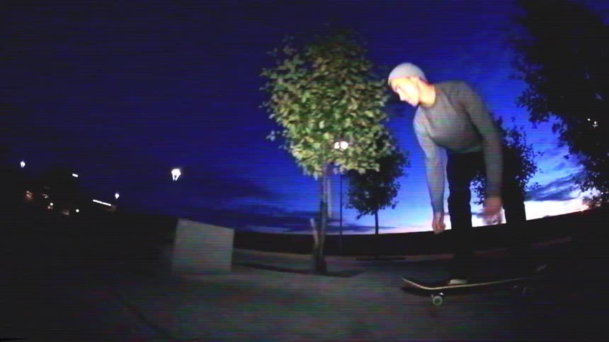 Slow motion fisheye footage shows a skateboarder doing a kickflip and then grinding on a ledge in a city park at dusk