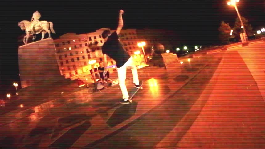 A young man skateboards in slow motion across a city plaza at night in this vintage-style footage