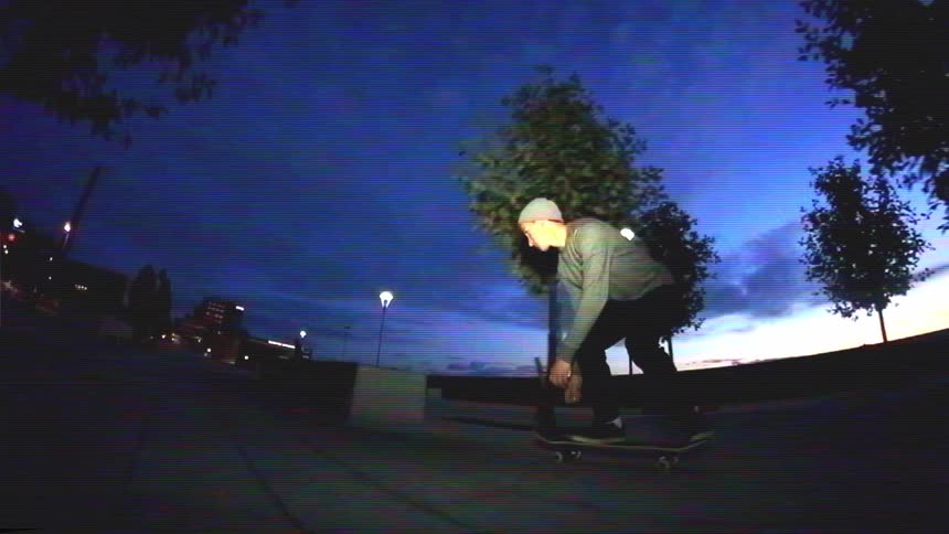 A skateboarder performs a slow-motion manual trick on a concrete ledge in an urban park at dusk