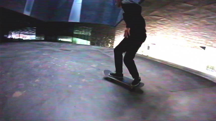 A lone skateboarder carves in slow motion through a dark, geometrically designed urban underpass