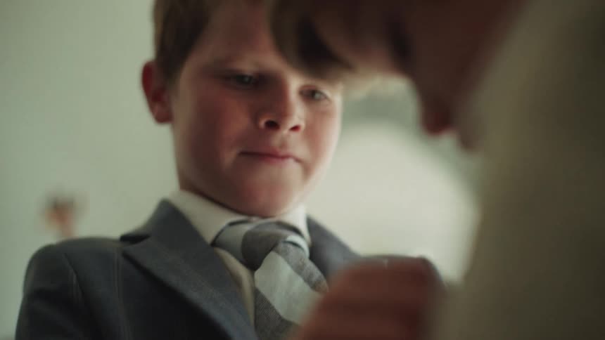 A young boy watches intently as his brother helps him get ready in his suit and tie for a special occasion