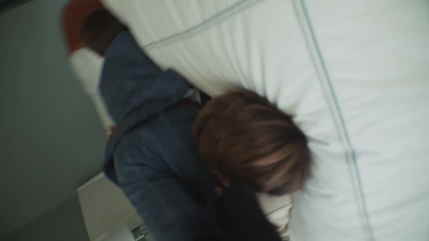 Two brothers in formal suits laugh while playfully wrestling on a bed in a chaotic slow-motion shot