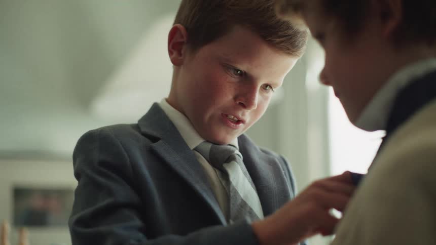 A young boy in a suit carefully adjusts his brother's tie in a heartwarming slow-motion close-up