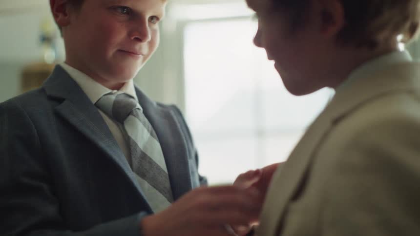 An older brother helps his younger brother get dressed in his suit and tie for a special occasion