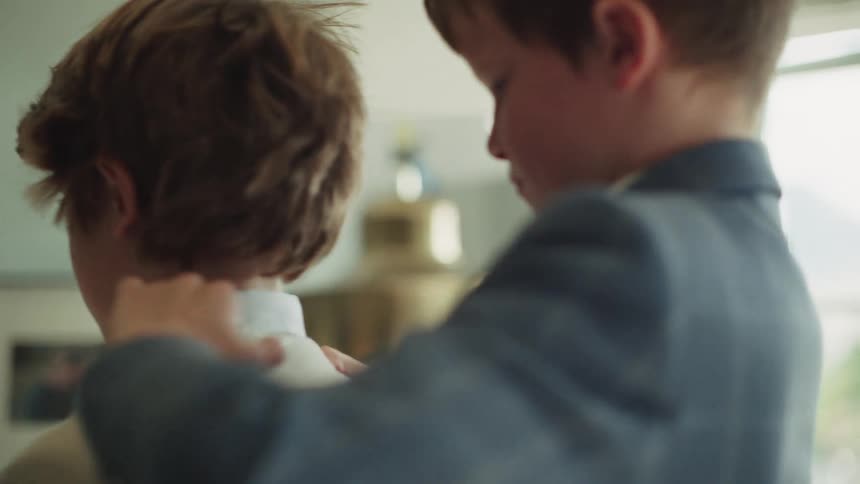 A caring young boy helps his brother or friend adjust his suit jacket collar in a warmly lit room