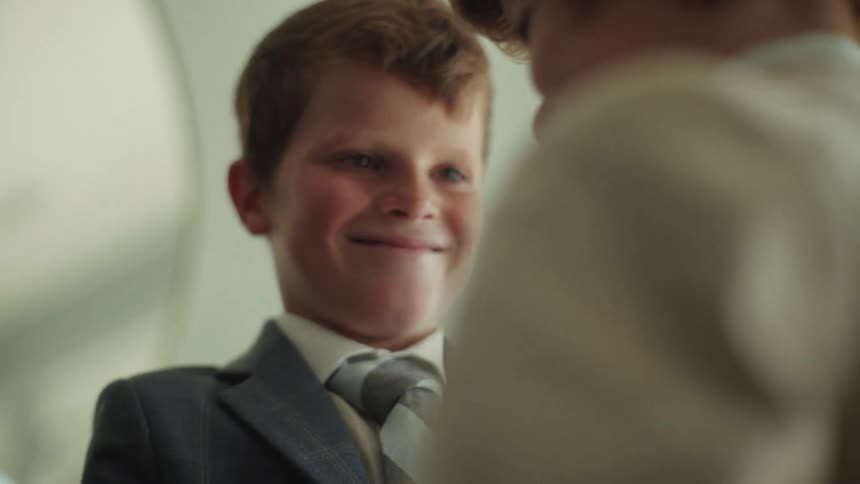 Close up of a cute red-haired boy in a suit and tie smiling as his brother helps him get ready