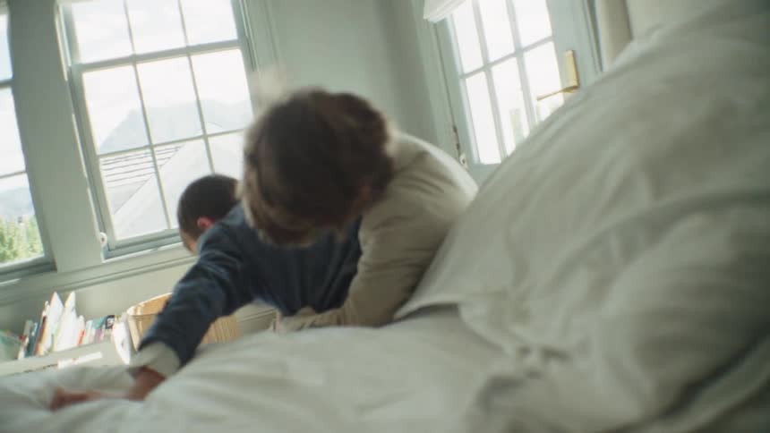 Two energetic young brothers in suits laugh and wrestle playfully on a bed in slow motion