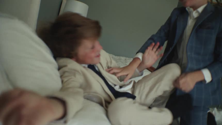 In slow motion, two well-dressed young brothers joyfully jump and wrestle on a bed in a stylish bedroom