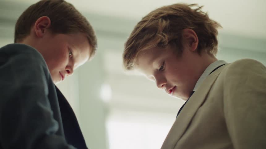 A young boy lovingly helps his brother adjust his tie and suit jacket as they get ready for a special occasion