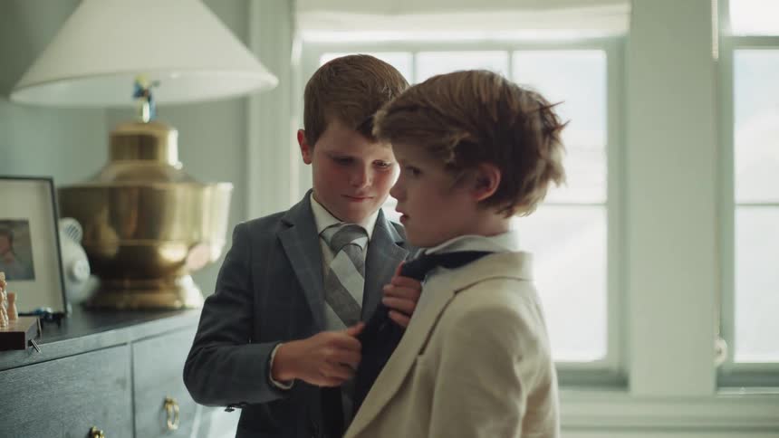 An older brother helps his younger brother get dressed up in a suit and tie for a formal event