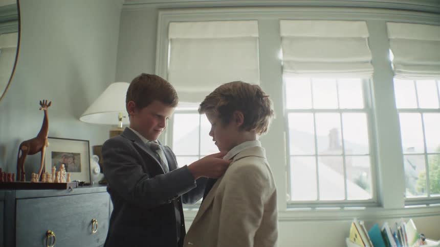 A caring young boy helps his brother adjust his suit and tie as they get ready together in their sunlit bedroom