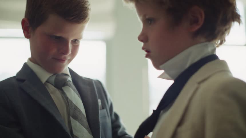 An older brother helps his younger brother tie his polka-dot necktie as they get dressed in suits for a formal event