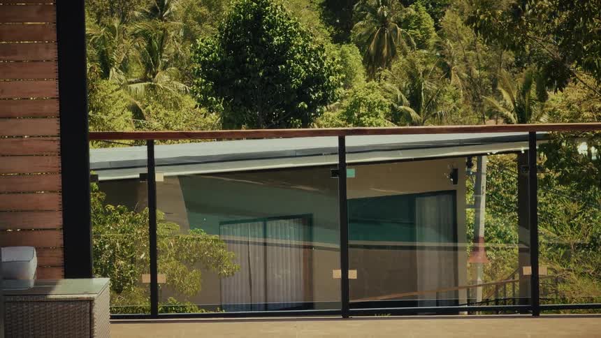 A serene view from a modern balcony with a glass railing looking out over a lush tropical jungle on a sunny day