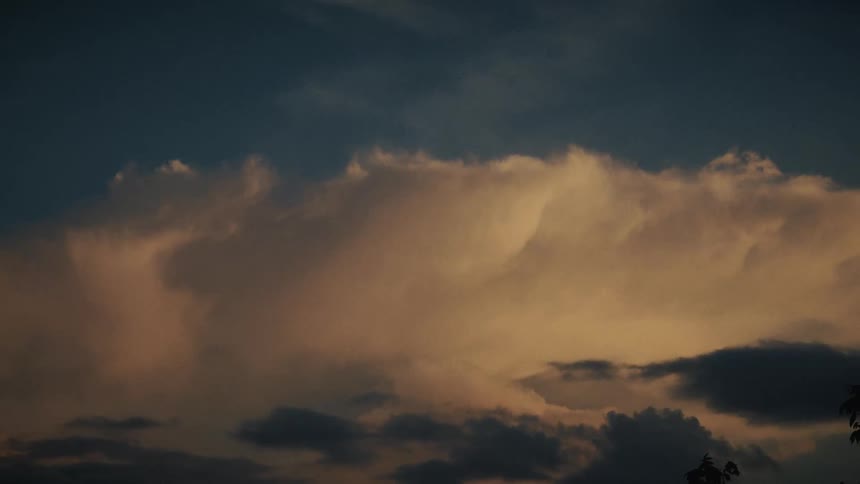 A beautiful and dramatic cloudscape glows with warm light at dusk as smaller, darker clouds float below