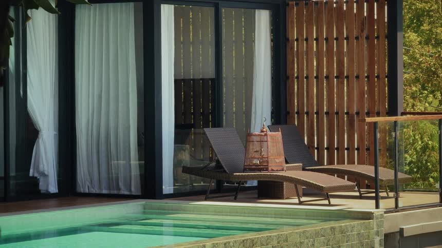 A tranquil view of a luxury hotel villa's private pool and patio with lounge chairs on a sunny day