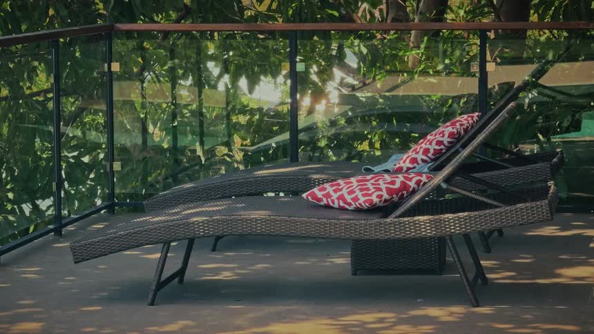 Peaceful scene of two rattan sun loungers on a tranquil balcony with a sun flare shining through the trees
