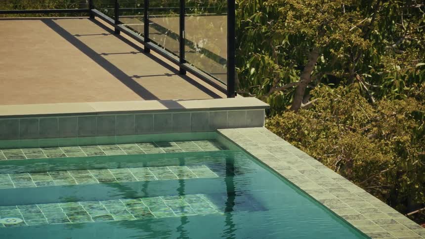 A peaceful view of a modern swimming pool's edge, with gentle ripples and a backdrop of lush trees