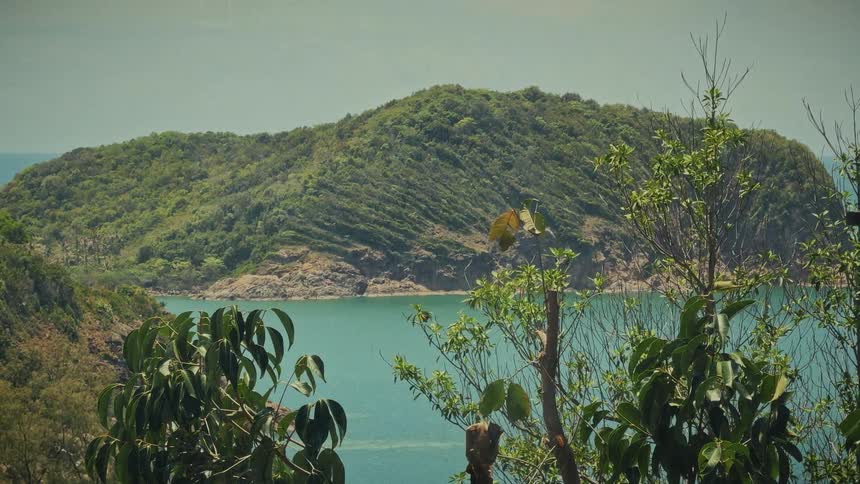A serene, vintage-style view of a lush tropical island with ridged green hillsides, surrounded by tranquil turquoise waters