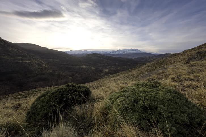 Sunbeams emerge through moving clouds over a vast, grassy mountain landscape in a time-lapse