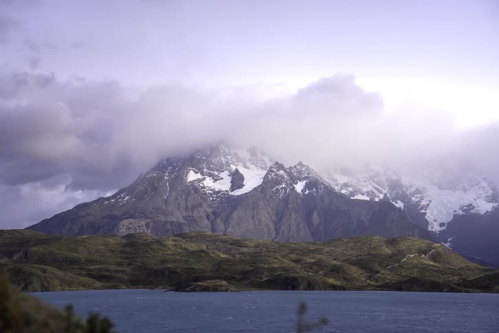 The majestic snow-capped peaks of Torres del Paine National Park in Patagonia are shrouded in dramatic clouds above a large lake