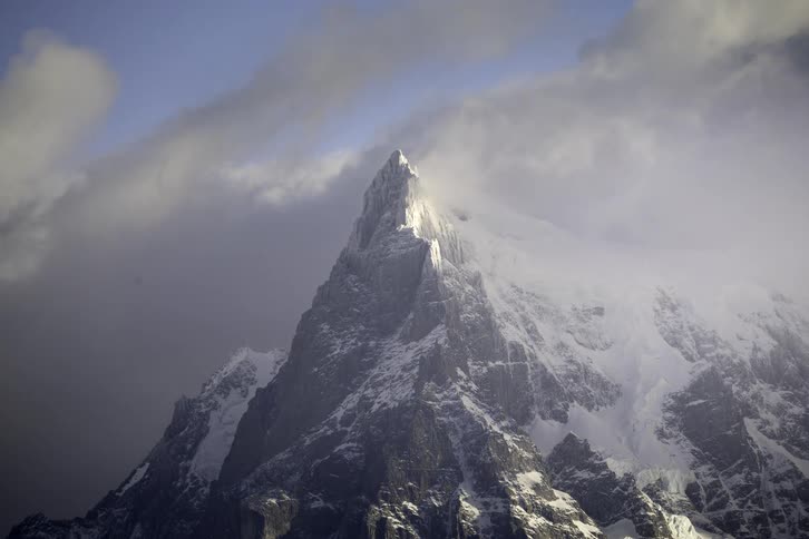 A dramatic time-lapse of clouds swirling around a majestic, snow-covered mountain peak as sunlight moves across its rugged face