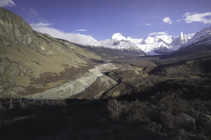 A stunning wide shot of a vast mountain valley with a winding river leading to the snow-capped Fitz Roy range in Patagonia