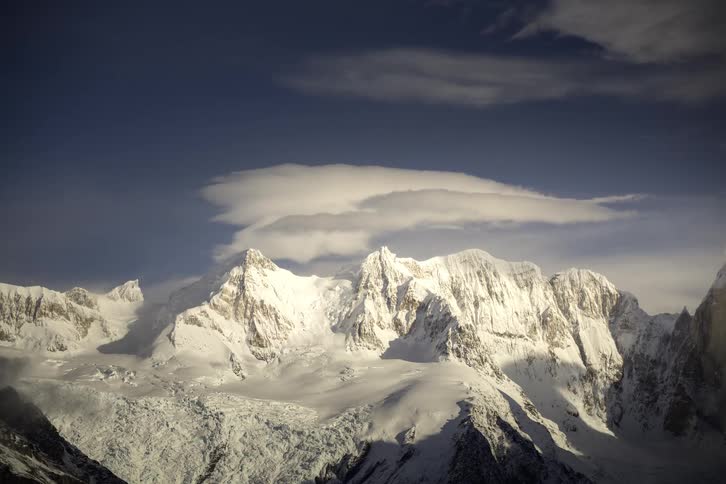 A majestic time-lapse of a lenticular cloud formation floating over a vast, snow-covered mountain range