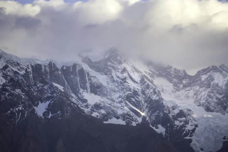 Dramatic clouds roll over the majestic, snow-covered peaks of a vast mountain range