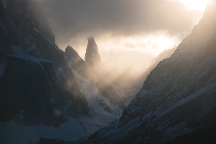 Golden light breaks through dark, stormy clouds, creating stunning light rays over a majestic, frozen mountain landscape