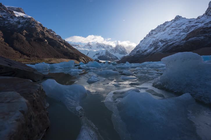 A majestic timelapse of clouds and sun moving over a glacial lake filled with icebergs at the foot of the snow-covered Fitz Roy mountain in Patagonia