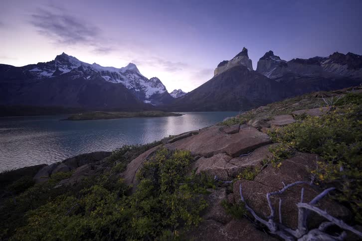 A stunning twilight timelapse moves over rocky terrain towards the snow-capped mountains and pristine lake of Torres del Paine National Park